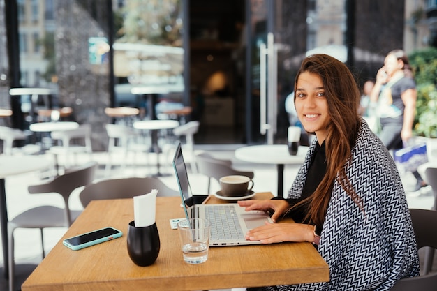 Foto gratuita retrato de una joven y bella mujer trabaja en una computadora portátil portátil, encantadora estudiante con net-book mientras está sentado en la cafetería