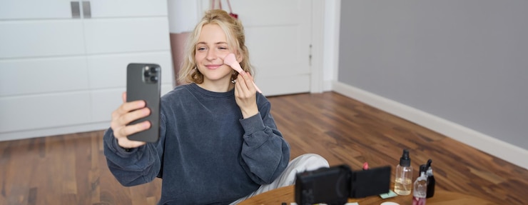 Foto gratuito retrato de una joven blogger de belleza grabando un vlog en su dormitorio haciendo un tutorial de maquillaje para