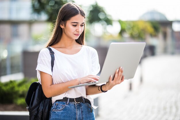 Retrato de joven blogger feliz con portátil moderno al aire libre