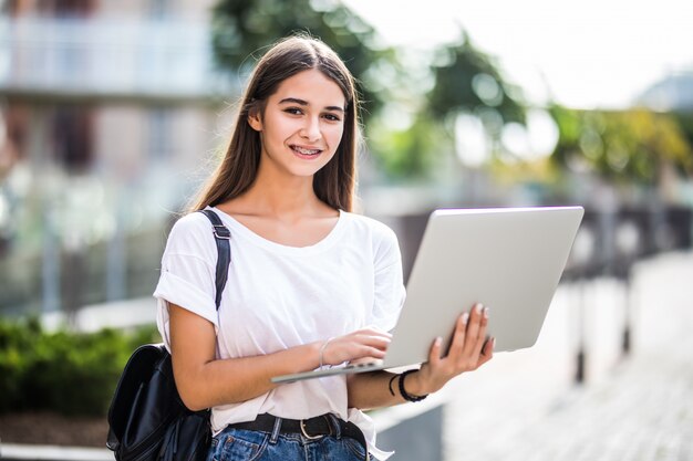 Retrato de joven blogger feliz con portátil moderno al aire libre