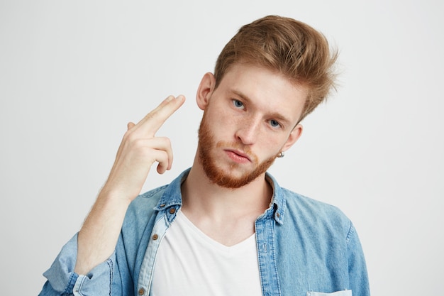 Retrato de joven brutal con barba haciendo pistola de mano.