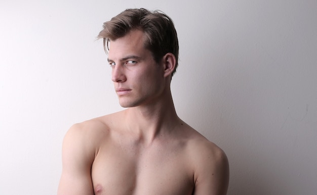 Retrato de un joven sin camisa de pie contra una pared blanca