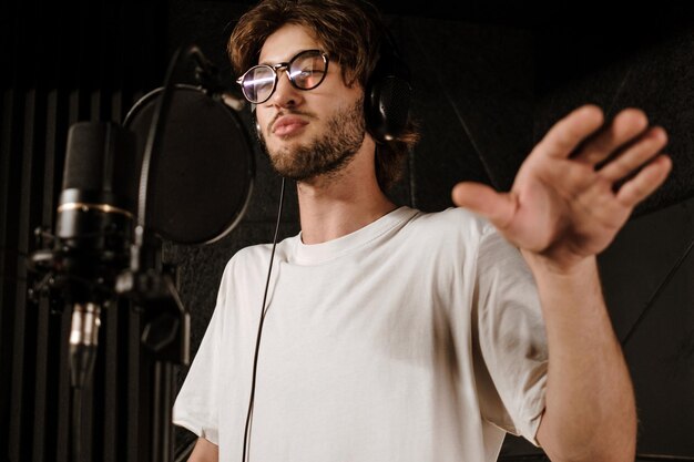 Retrato de joven cantante en auriculares cantando durante la grabación de una nueva canción en un estudio moderno