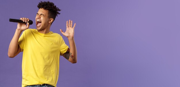 Retrato de joven cantante hispano apasionado y despreocupado con rastas y tatuajes que alcanzan la nota más alta