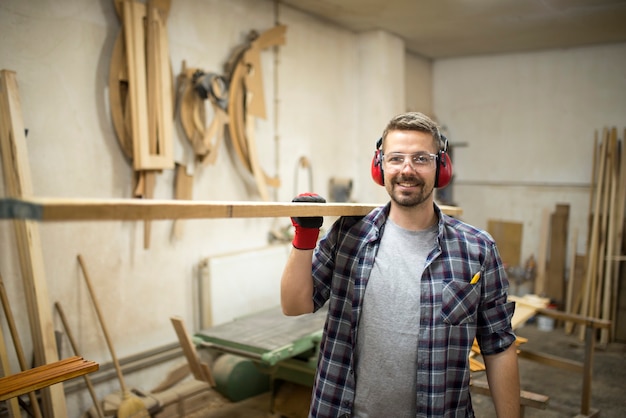 Retrato de joven carpintero sosteniendo madera en su taller de carpintería