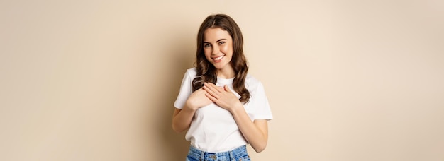 Retrato de una joven caucásica con las manos en el corazón y sonriendo soñando despierto pensando en algo del corazón