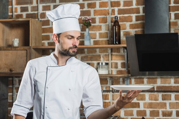Retrato de joven cocinero profesional masculino sosteniendo un plato blanco vacío en la mano