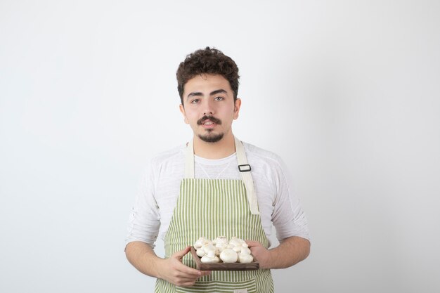 Retrato de joven cocinero sosteniendo setas crudas en blanco
