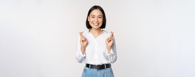 Retrato de una joven coreana, una chica asiática, cruza los dedos y reza pidiendo un deseo anticipando la espera