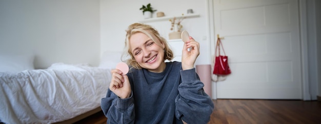 Retrato de una joven creadora de contenido que muestra productos de maquillaje de belleza ante la cámara sentada en el suelo en