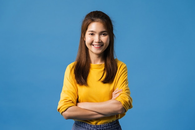 Retrato de joven dama de Asia con expresión positiva, brazos cruzados, sonrisa amplia, vestida con ropa casual y mirando a cámara sobre fondo azul. Feliz adorable mujer alegre se regocija con el éxito.