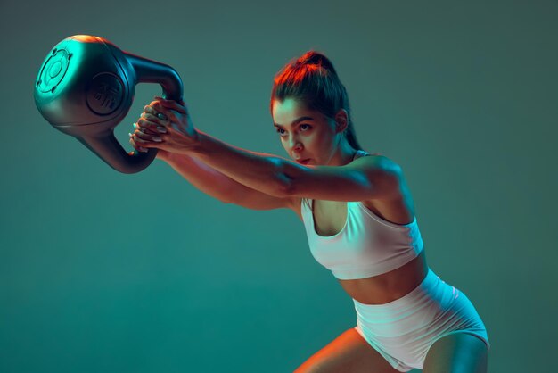 Retrato de joven deportista haciendo sentadillas con peso aislado sobre fondo verde en neón