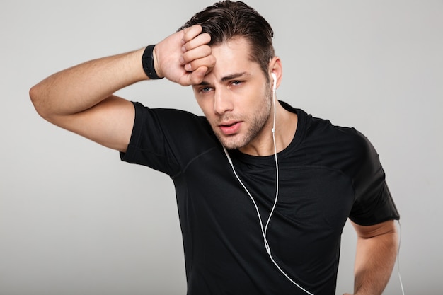 Retrato de un joven deportista sudoroso cansado en auriculares