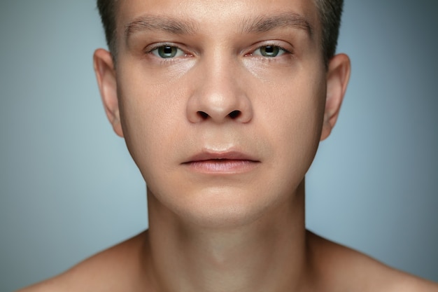 Retrato de joven descamisado aislado en la pared gris. Modelo masculino caucásico sano que mira la cámara y que presenta. Concepto de salud y belleza de los hombres, cuidado personal, cuidado del cuerpo y de la piel.