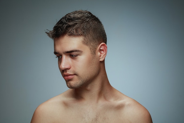 Retrato de joven descamisado aislado sobre fondo gris. Modelo masculino caucásico sano que mira el lado y que presenta.