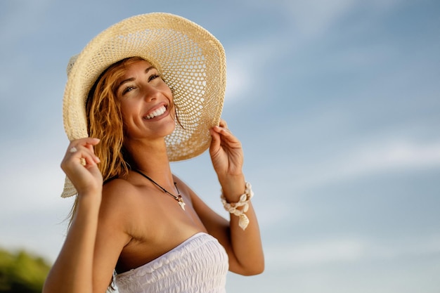 Retrato de una joven despreocupada con sombrero de paja disfrutando en verano y mirando a la cámara