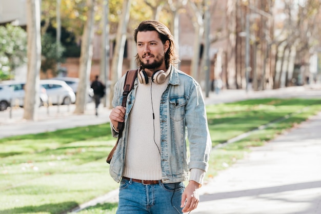 Retrato de un joven elegante con auriculares alrededor de su cuello caminando en el parque