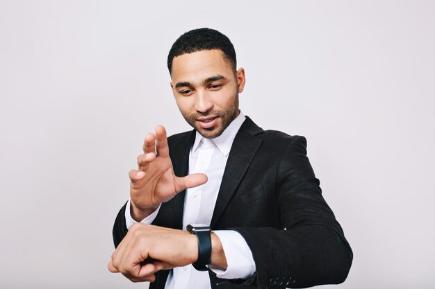 Retrato de joven elegante con camisa blanca, chaqueta negra divirtiéndose con reloj sobre fondo blanco. Tiempo mágico, trabajador inteligente, empresario exitoso, reunión, trabajo, alegría