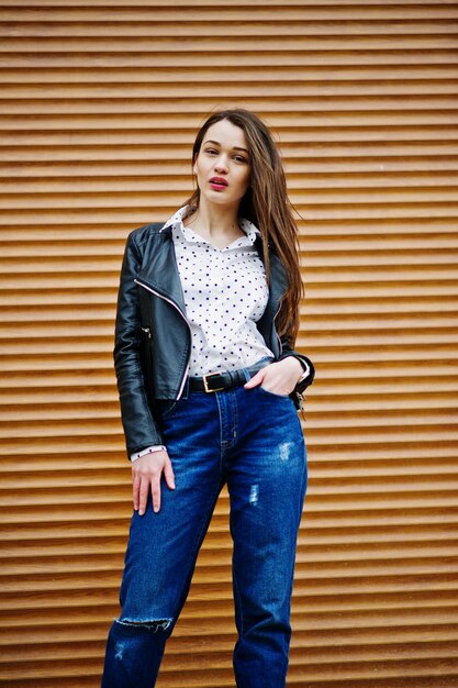 Retrato de una joven elegante vestida con chaqueta de cuero y jeans rasgados textura de obturador de fondo Estilo de modelo de moda callejera