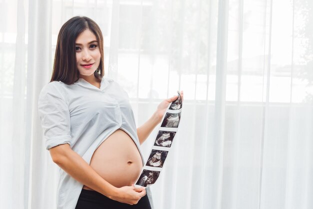 Retrato de una joven embarazada asiática adulta sosteniendo una foto de ultrasonido con feliz