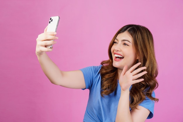 Retrato de una joven emocionada que usa una videollamada casual en un teléfono inteligente aislado sobre fondo rosa