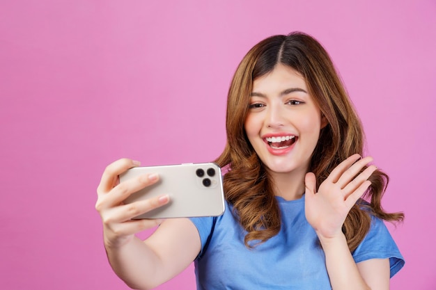 Retrato de una joven emocionada que usa una videollamada casual en un teléfono inteligente aislado sobre fondo rosa