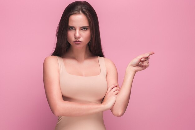 El retrato de la joven con emociones tristes en estudio rosa. La mujer apuntando a la derecha con el dedo