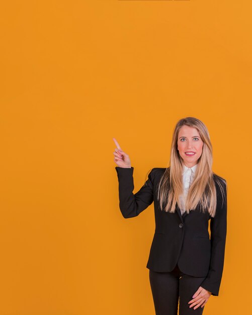 Retrato de una joven empresaria apuntando su dedo contra un telón de fondo naranja