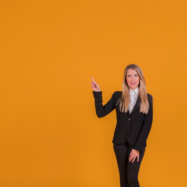 Retrato de una joven empresaria apuntando su dedo sobre un fondo naranja