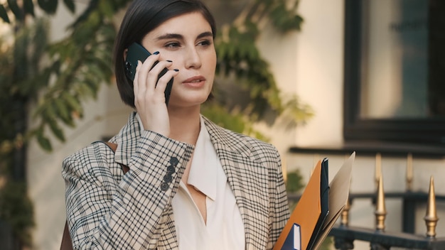 Retrato de una joven empresaria hablando por teléfono esperando una reunión de negocios en una acogedora calle de la ciudad Agente inmobiliario moderno esperando clientes al aire libre