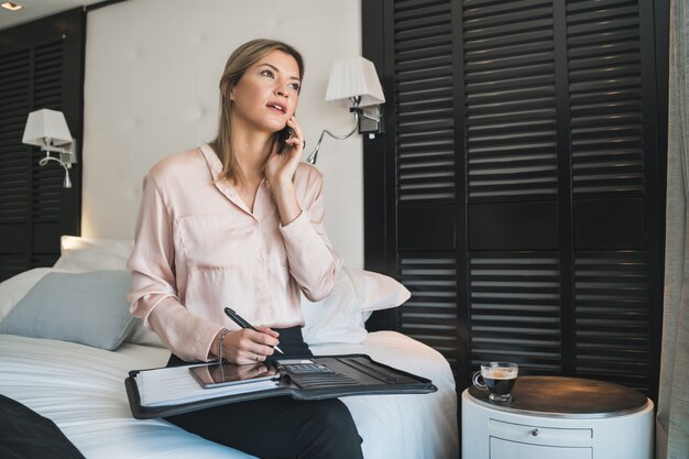 Retrato de joven empresaria hablando por teléfono en la habitación del hotel. Concepto de viajes de negocios.