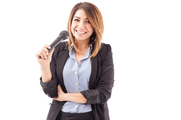 Retrato de una joven empresaria hispana sosteniendo un micrófono durante un seminario y sonriendo