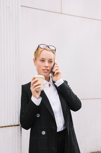 Retrato de una joven empresaria de pie contra la pared hablando por teléfono celular