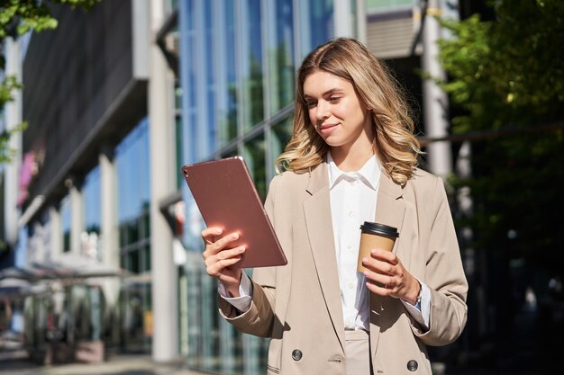 Retrato de una joven empresaria segura de sí misma en la calle bebe su café y mira los trabajos de la tableta en h