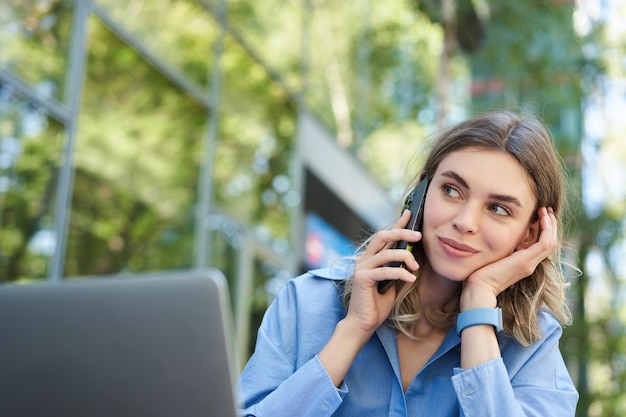 Retrato de una joven empresaria sentada afuera en el parque hablando por teléfono móvil usando una laptop joven w