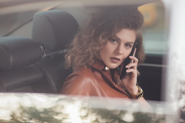 Retrato de joven empresaria sentada en el coche y hablando por teléfono inteligente