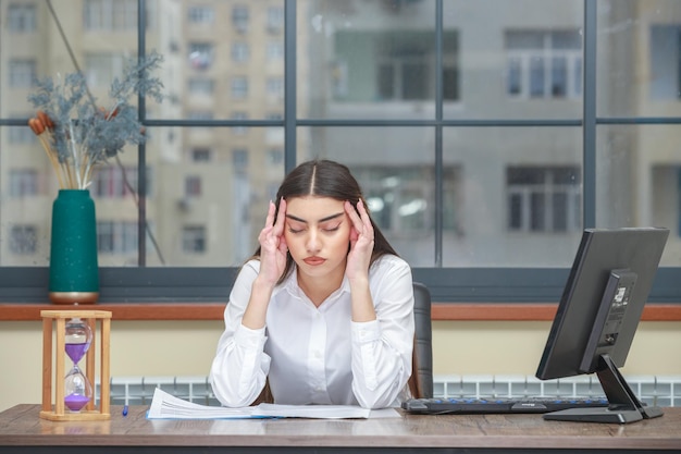 Retrato de una joven empresaria sentada en el escritorio y llevándose las manos a la cabeza