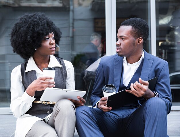 Retrato de un joven empresario africano y empresaria sentados juntos fuera de la oficina