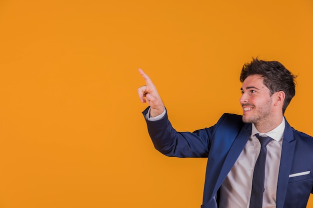 Retrato de un joven empresario apuntando su dedo contra un telón de fondo naranja