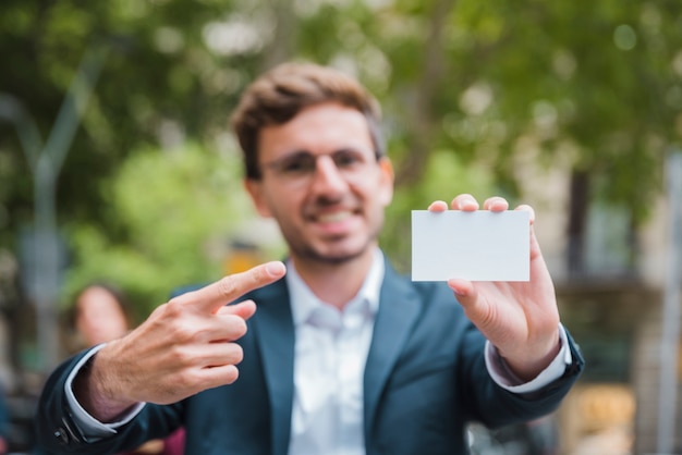 Retrato de un joven empresario desenfocado que apunta su dedo hacia la tarjeta de visita blanca