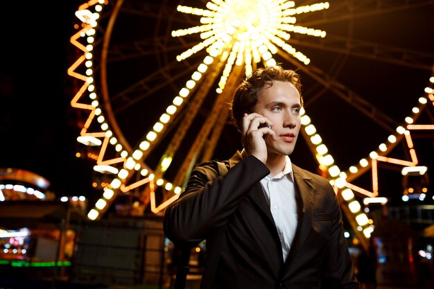 Retrato de joven empresario exitoso sobre el parque de atracciones nocturno. DOF superficial