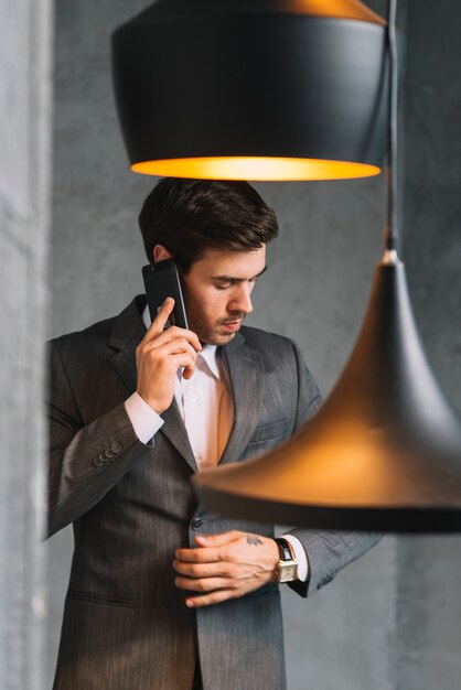 Retrato de un joven empresario hablando por teléfono inteligente con luz colgante en primer plano
