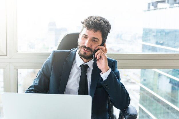 Retrato de joven empresario hablando por teléfono móvil cerca de la ventana