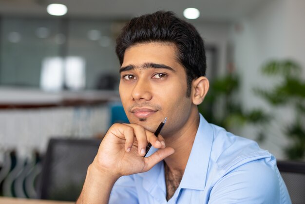 Retrato de joven empresario indio o estudiante sentado con pluma