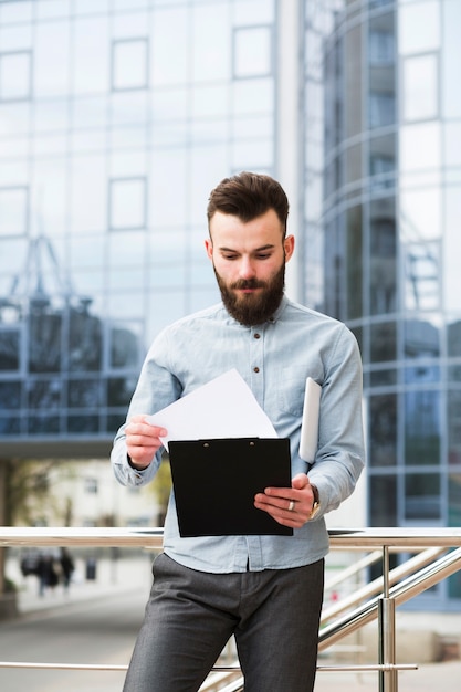 Retrato de un joven empresario revisando el documento frente al edificio de oficinas