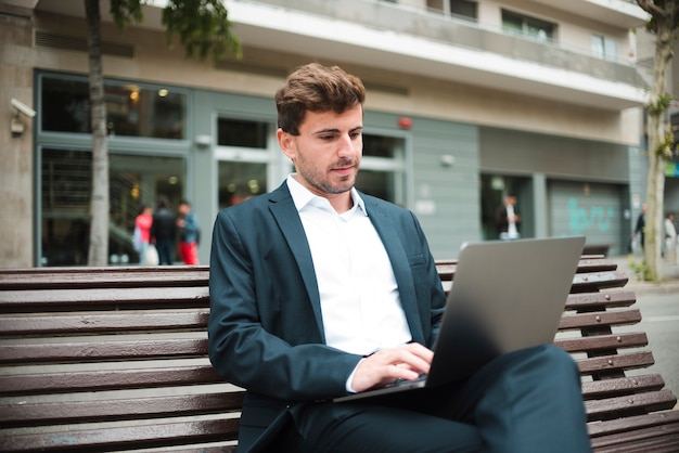 Retrato de un joven empresario sentado en el banco usando laptop