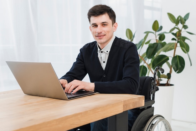 Retrato de un joven empresario sonriente sentado en silla de ruedas usando laptop