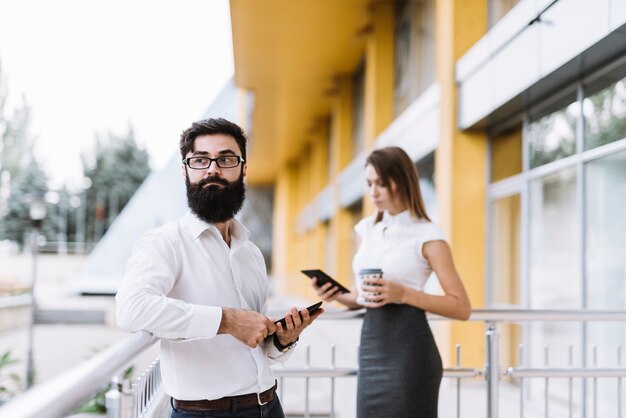 Retrato de joven empresario sosteniendo tableta digital con empresaria de pie en el fondo
