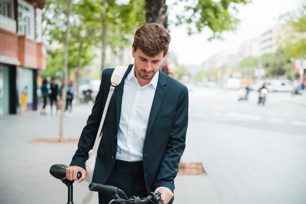 Retrato de un joven empresario con su bicicleta de pie en la calle