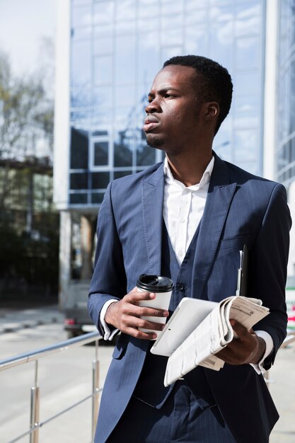 Retrato de un joven empresario con tableta digital; taza de café desechable y periódico